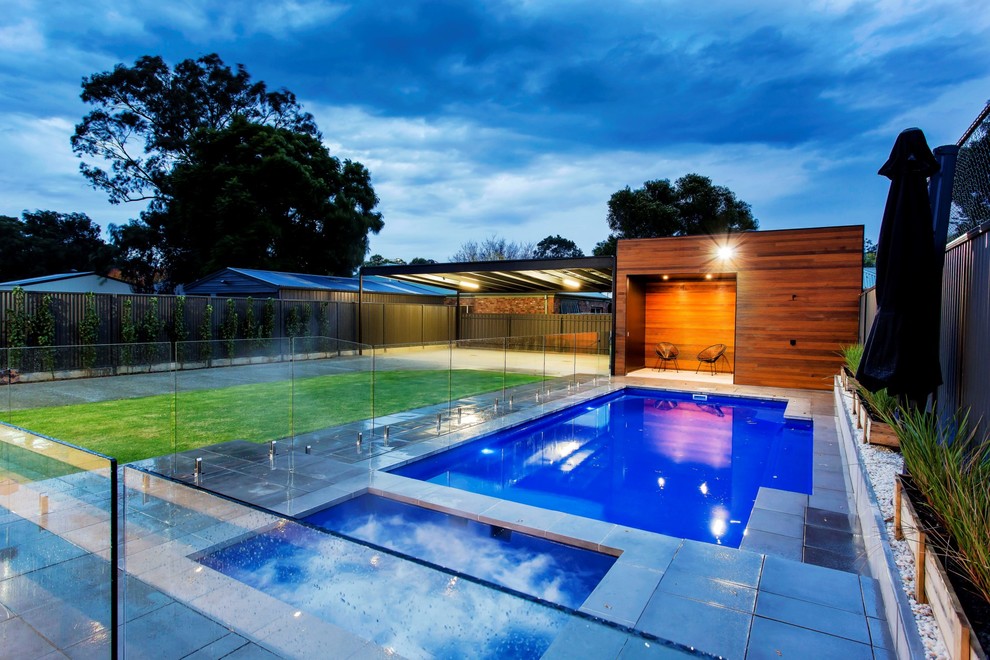 Ispirazione per una grande piscina monocorsia minimal rettangolare dietro casa con una vasca idromassaggio e pavimentazioni in pietra naturale