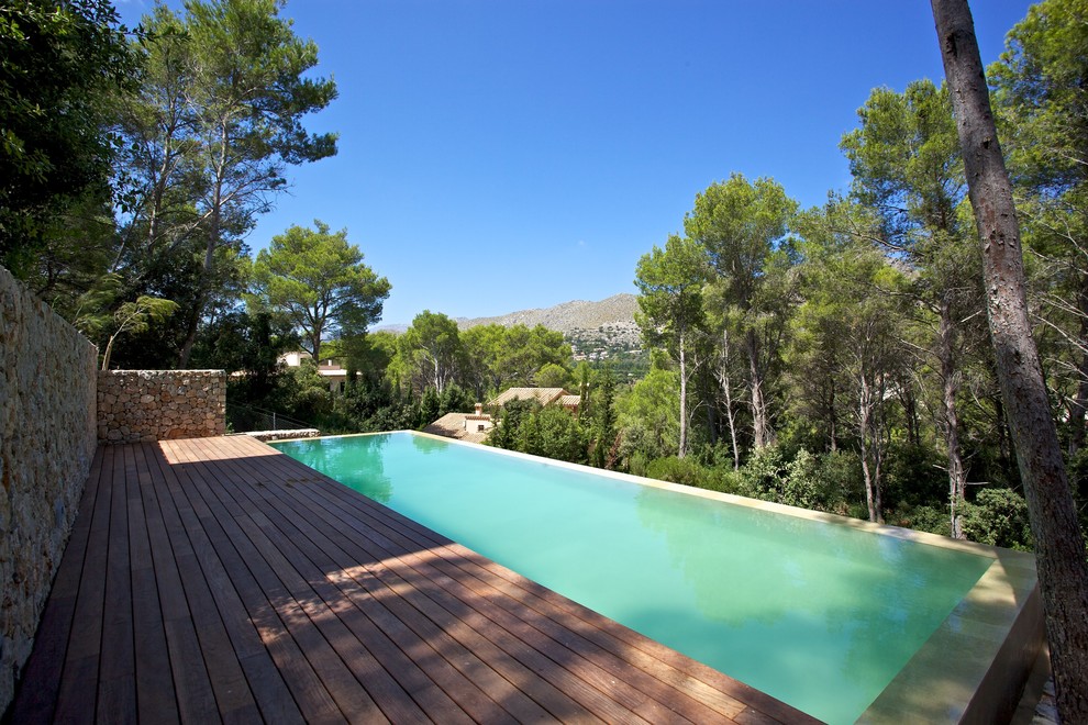 Large rustic roof custom shaped infinity swimming pool in Other with decking.