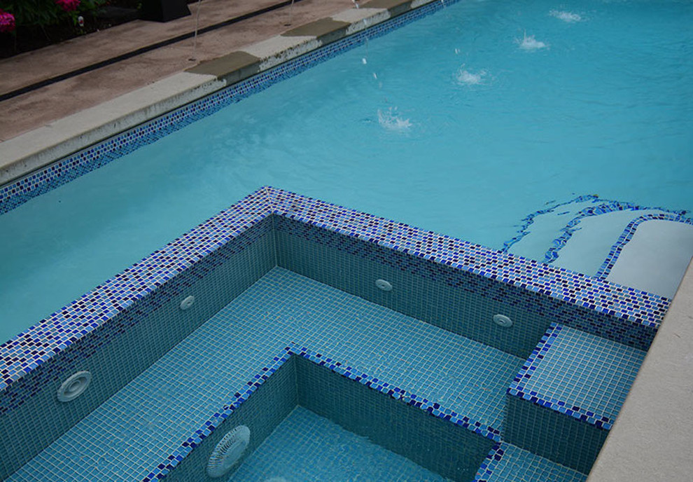 Esempio di una piscina monocorsia contemporanea rettangolare di medie dimensioni e dietro casa con una vasca idromassaggio e lastre di cemento