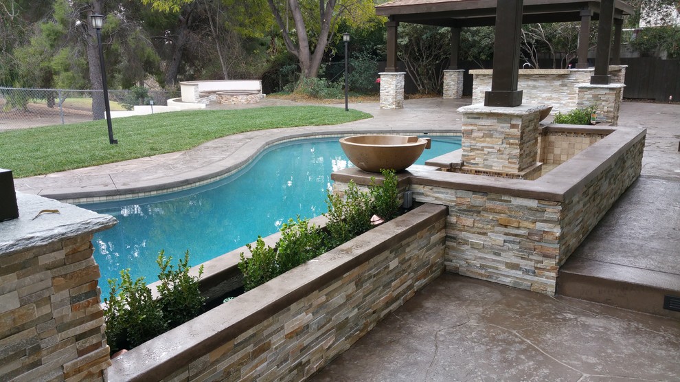 This is an example of a large modern back custom shaped above ground swimming pool in Los Angeles with a water feature and stamped concrete.