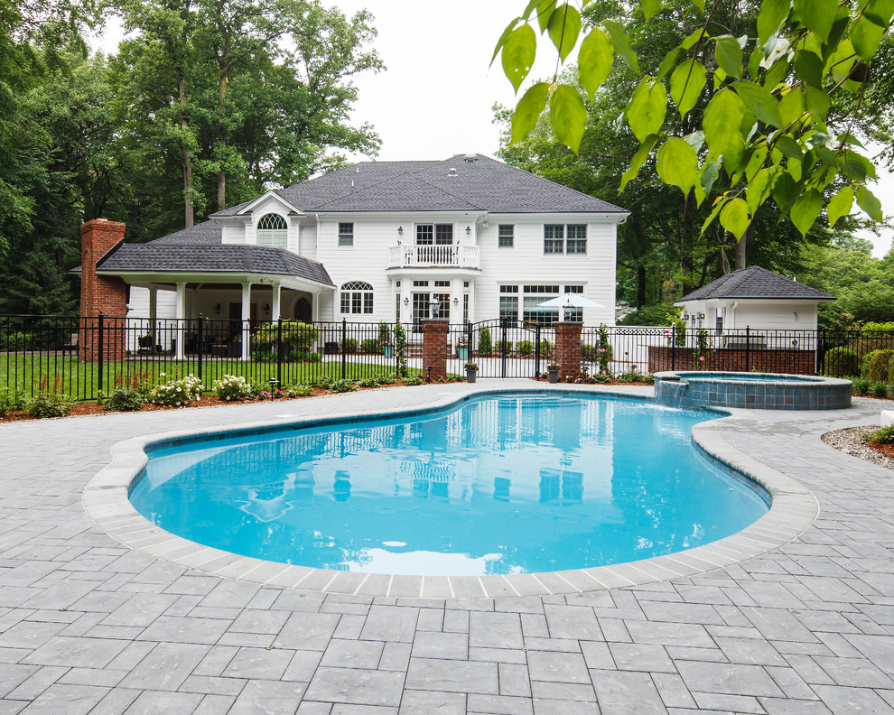 Modelo de piscina alargada clásica de tamaño medio tipo riñón en patio trasero con adoquines de hormigón