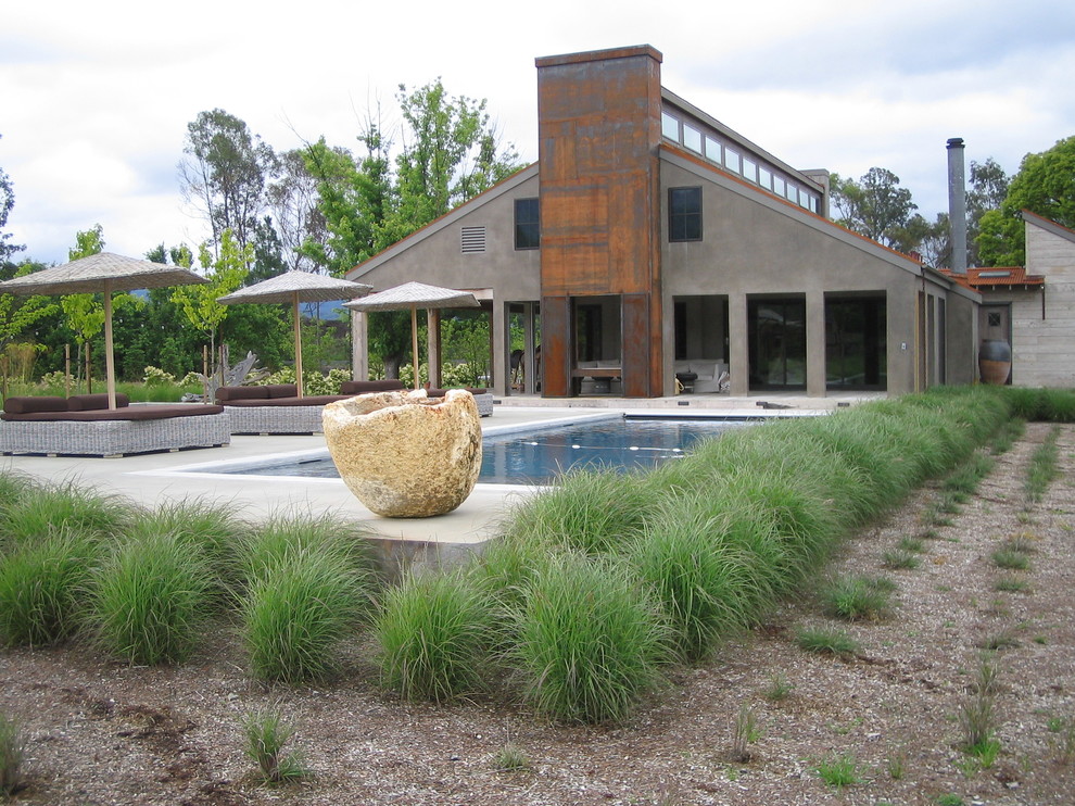 Foto de piscina alargada campestre de tamaño medio rectangular en patio trasero con losas de hormigón