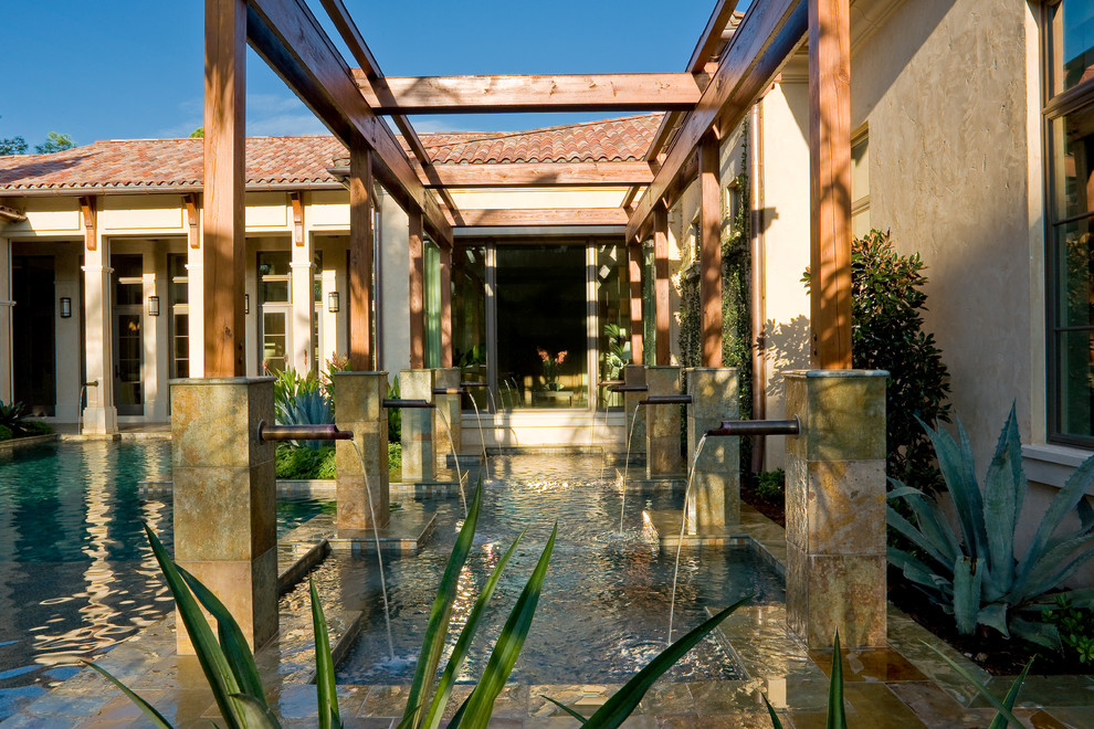 Imagen de piscina con fuente mediterránea grande a medida en patio trasero con adoquines de piedra natural