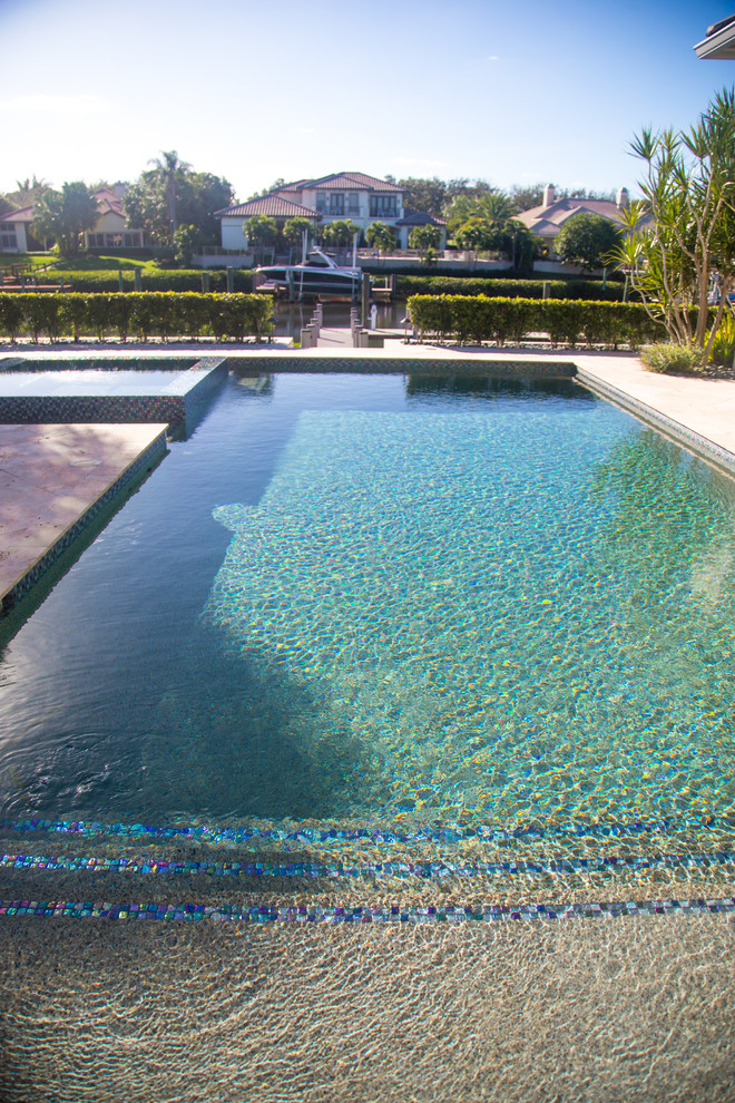 На фото: большой прямоугольный бассейн-инфинити на заднем дворе в средиземноморском стиле с джакузи и покрытием из плитки