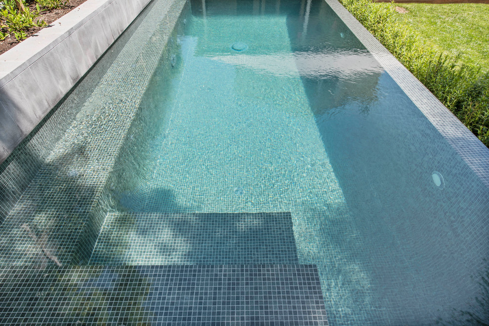 На фото: наземный, прямоугольный бассейн среднего размера на заднем дворе в стиле модернизм с покрытием из плитки
