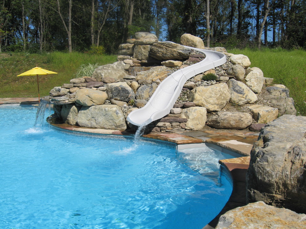 Réalisation d'une grande piscine arrière et naturelle tradition sur mesure avec un toboggan et des pavés en pierre naturelle.