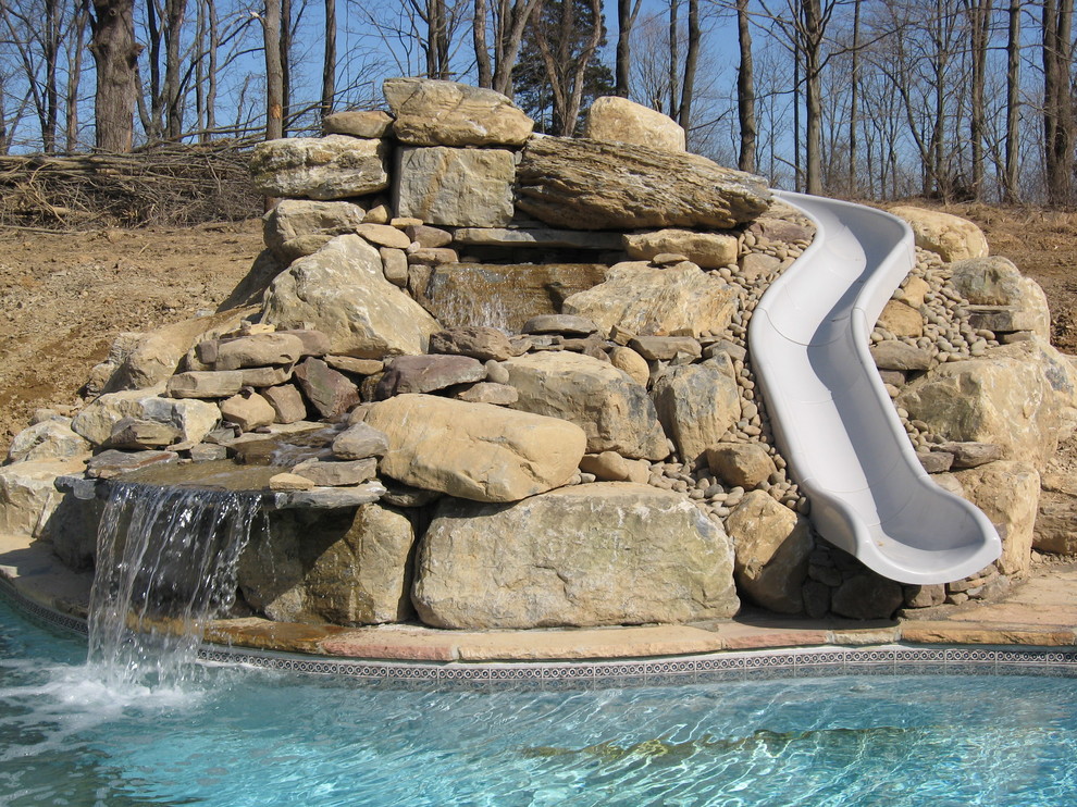 Foto de piscina con tobogán tradicional grande a medida en patio trasero con adoquines de piedra natural