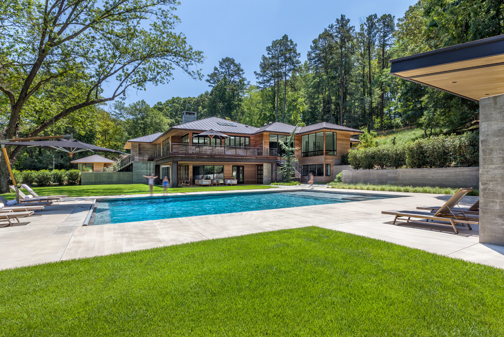 Ejemplo de casa de la piscina y piscina actual grande rectangular con losas de hormigón