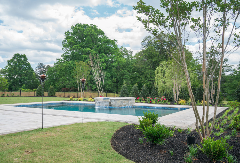 Modelo de piscinas y jacuzzis alargados clásicos grandes rectangulares en patio trasero con adoquines de hormigón
