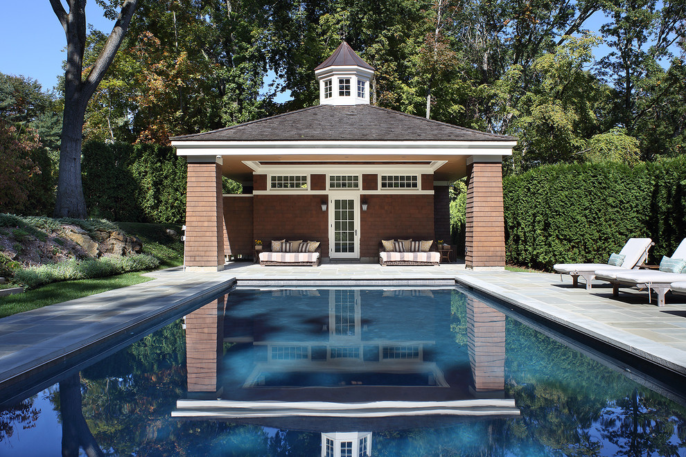 Modelo de piscina tradicional grande rectangular en patio trasero con adoquines de piedra natural