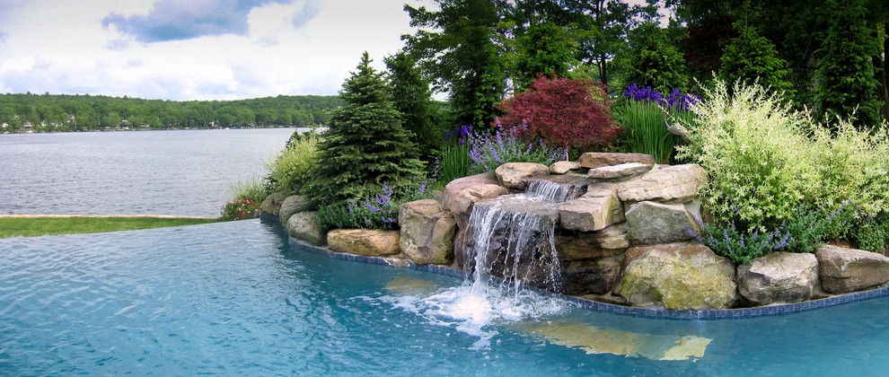 Exemple d'une piscine à débordement et arrière bord de mer de taille moyenne et sur mesure avec un point d'eau et des pavés en pierre naturelle.