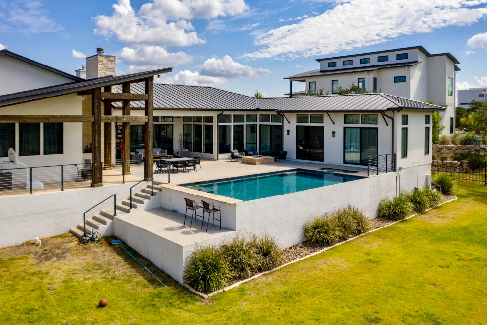 Esempio di un'ampia piscina a sfioro infinito moderna rettangolare dietro casa con lastre di cemento