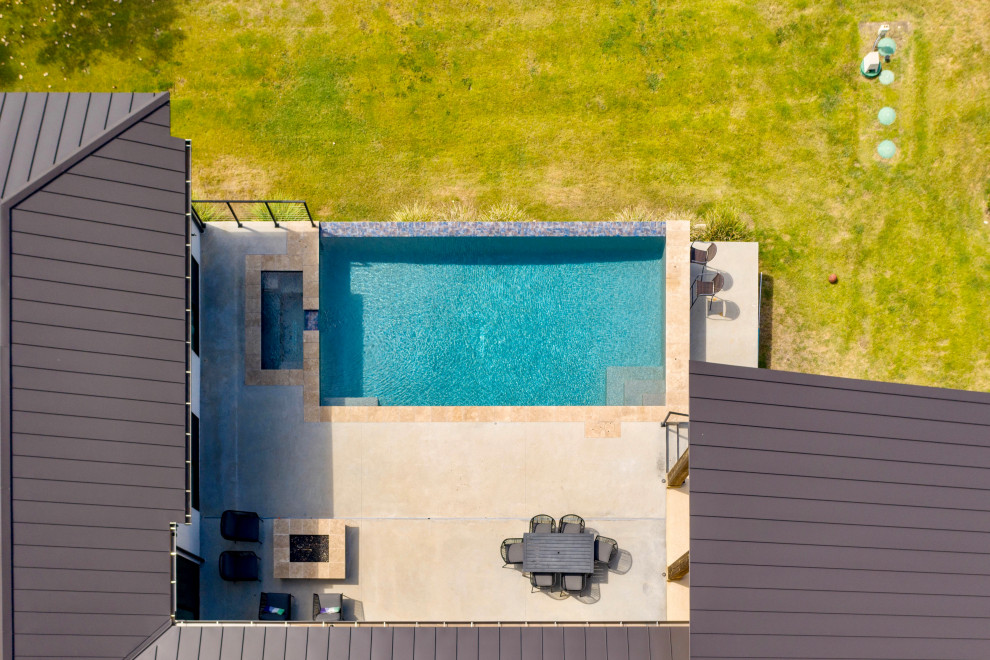 Idee per un'ampia piscina a sfioro infinito moderna rettangolare dietro casa con lastre di cemento