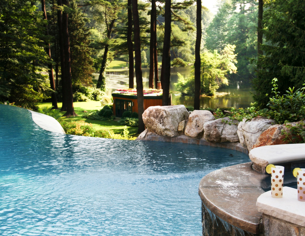 Example of a large mountain style backyard stone and custom-shaped infinity hot tub design in New York