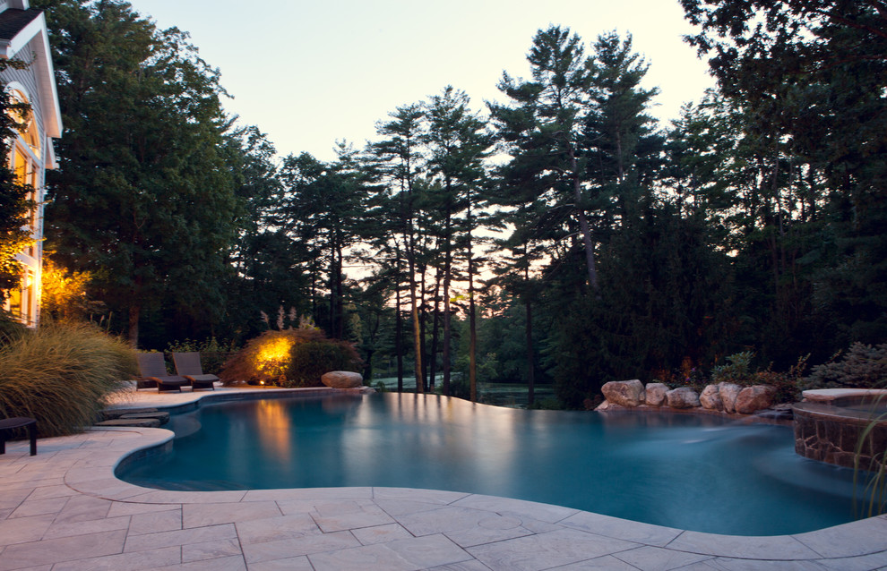 Inspiration for a large rustic back custom shaped infinity hot tub in New York with natural stone paving.