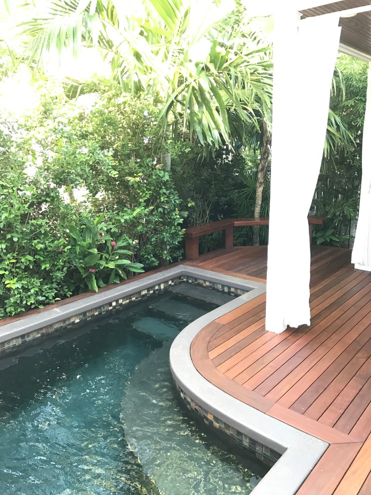 Aménagement d'une petite piscine arrière exotique en L avec un point d'eau et une terrasse en bois.