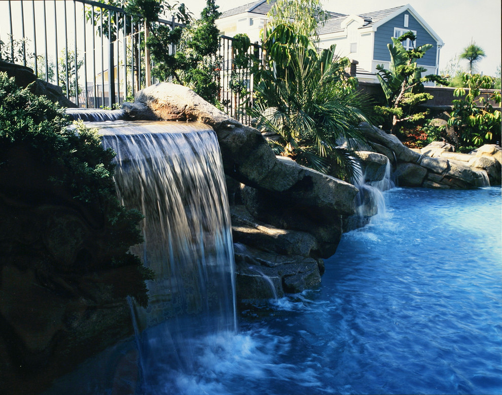 Imagen de piscina con tobogán tropical a medida en patio trasero con suelo de hormigón estampado