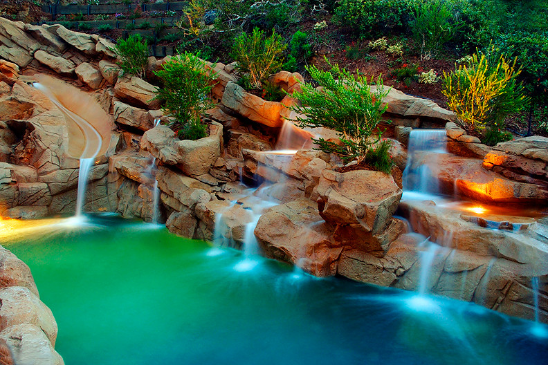 Expansive world-inspired back custom shaped swimming pool in Orange County with a water slide and stamped concrete.