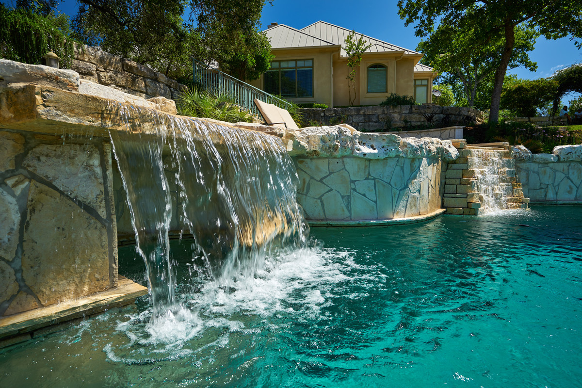 Cette image montre une grande piscine à débordement et arrière ethnique sur mesure avec un bain bouillonnant et des pavés en pierre naturelle.