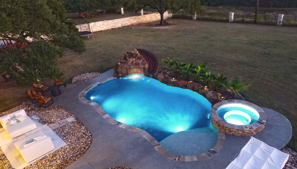 Idee per una grande piscina tropicale personalizzata dietro casa con un acquascivolo e lastre di cemento