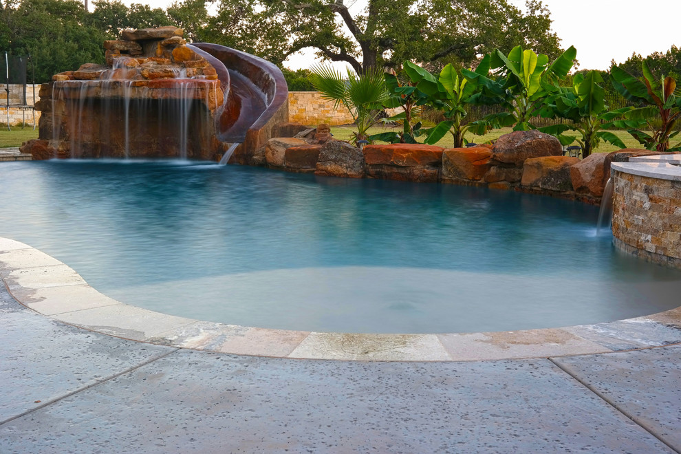 Immagine di una grande piscina tropicale personalizzata dietro casa con un acquascivolo e lastre di cemento