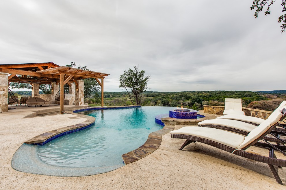 Expansive traditional back custom shaped infinity swimming pool in Austin with a water feature and stamped concrete.