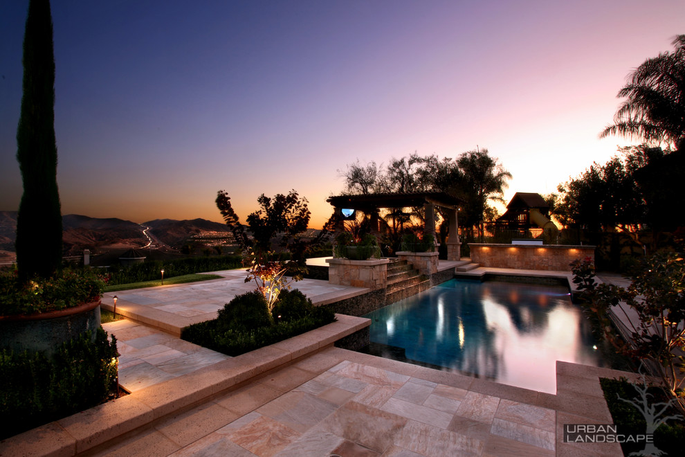 Inspiration for a large mediterranean back rectangular infinity hot tub in Orange County with natural stone paving.