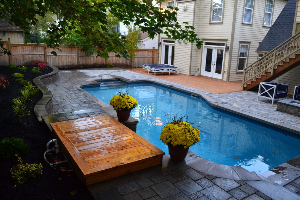 Imagen de piscina con fuente alargada actual grande a medida en patio trasero con adoquines de hormigón