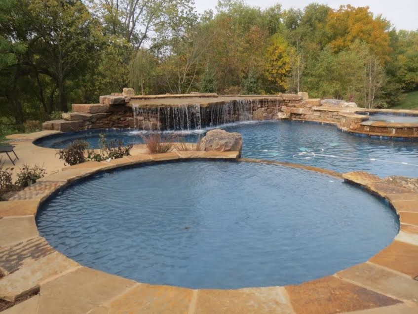 Inspiration for a large rustic back custom shaped swimming pool in Kansas City with a water feature and natural stone paving.