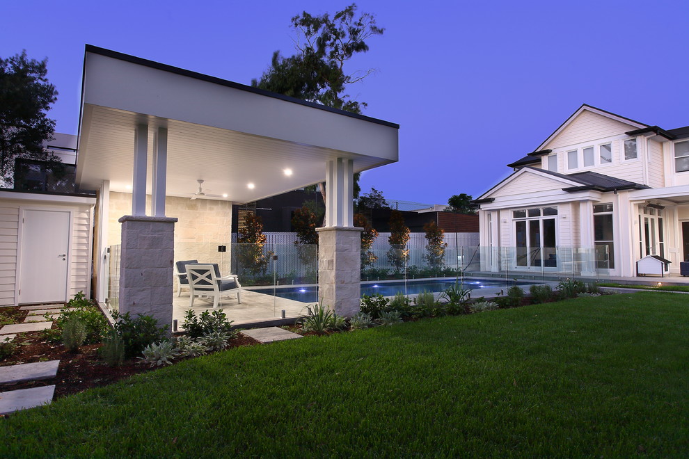 Modelo de casa de la piscina y piscina actual de tamaño medio rectangular en patio trasero con adoquines de piedra natural