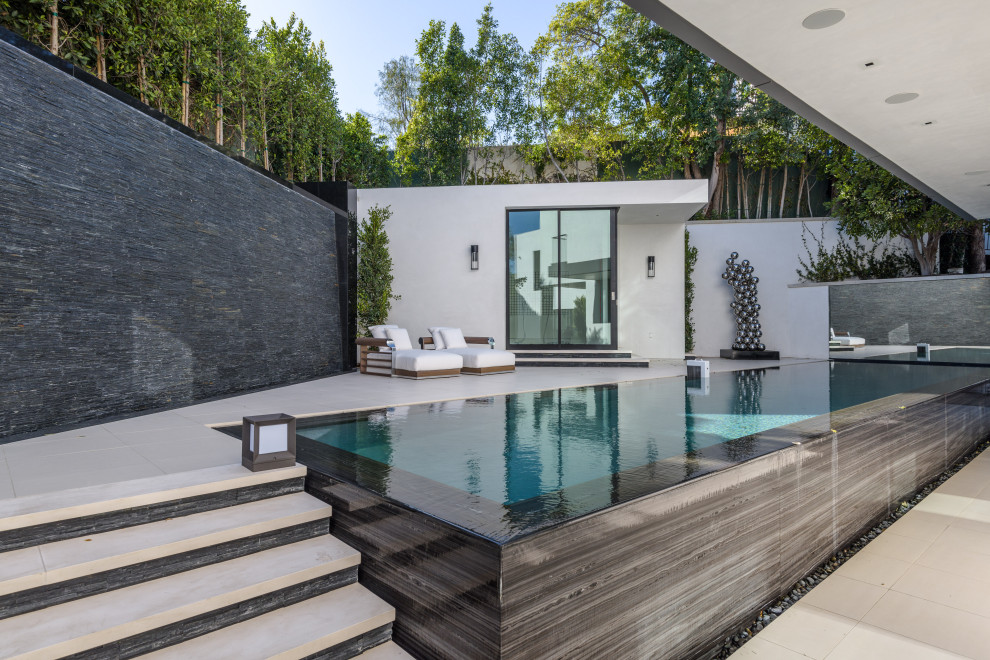 На фото: прямоугольный бассейн-инфинити среднего размера на заднем дворе в стиле модернизм с покрытием из плитки и домиком у бассейна