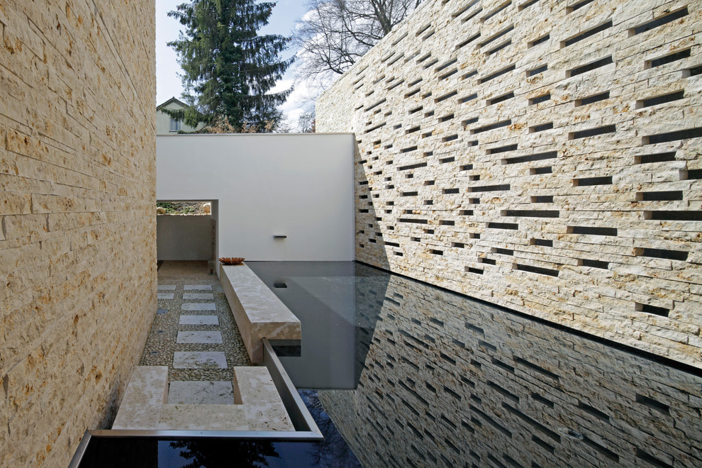 Esempio di una grande piscina a sfioro infinito minimalista a "L" in cortile con pavimentazioni in pietra naturale