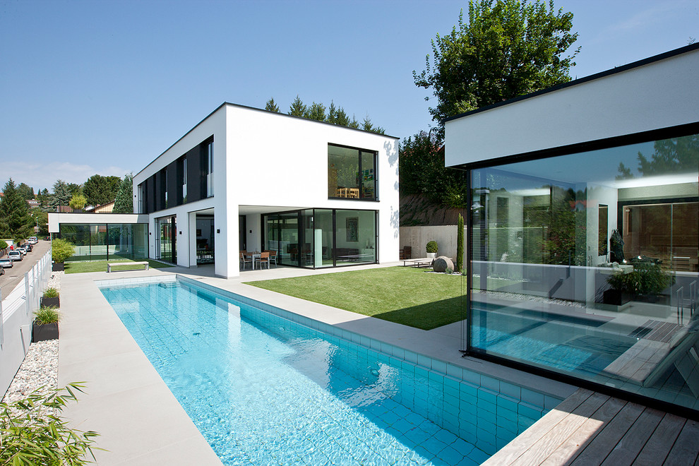 Imagen de casa de la piscina y piscina alargada actual grande rectangular en patio lateral con losas de hormigón
