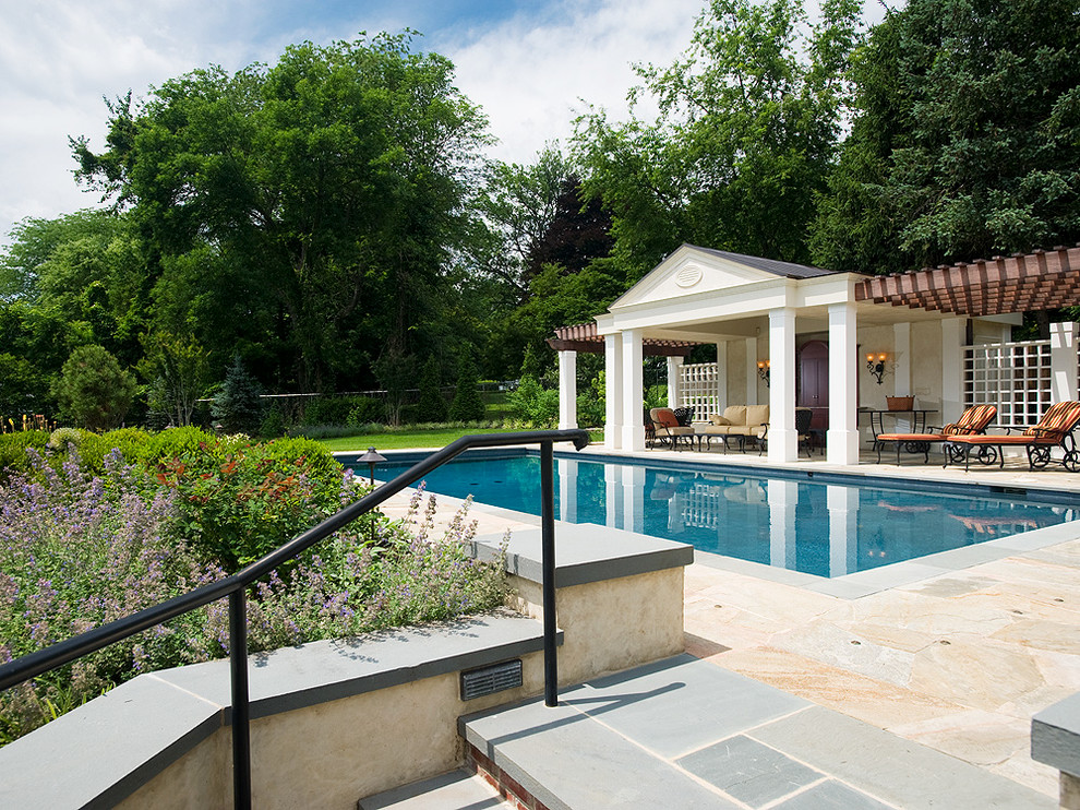 Ejemplo de casa de la piscina y piscina tradicional de tamaño medio rectangular en patio trasero con adoquines de piedra natural