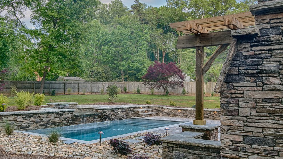 Modelo de piscina con fuente alargada de estilo de casa de campo de tamaño medio rectangular en patio trasero con adoquines de hormigón