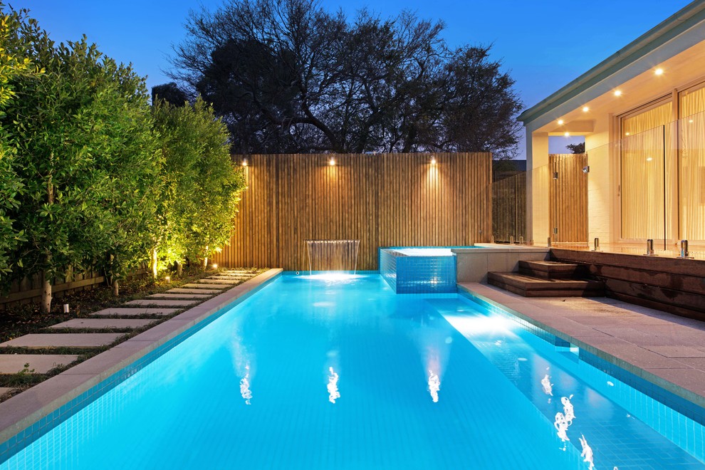 Diseño de piscina con fuente alargada minimalista de tamaño medio rectangular en patio trasero con adoquines de hormigón