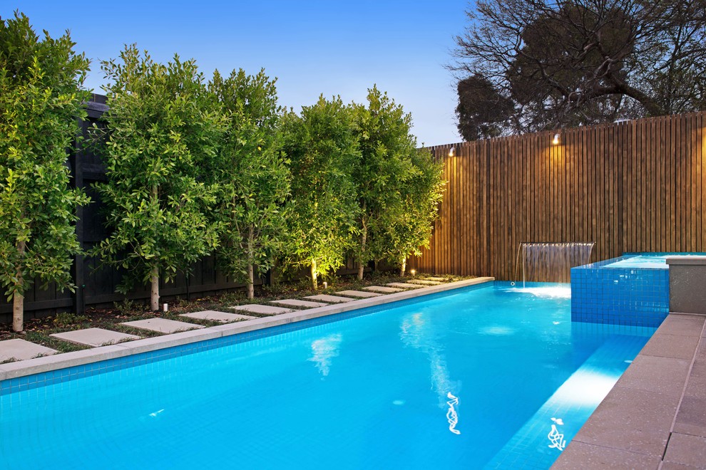 Modelo de piscina con fuente alargada moderna de tamaño medio rectangular en patio trasero con adoquines de hormigón