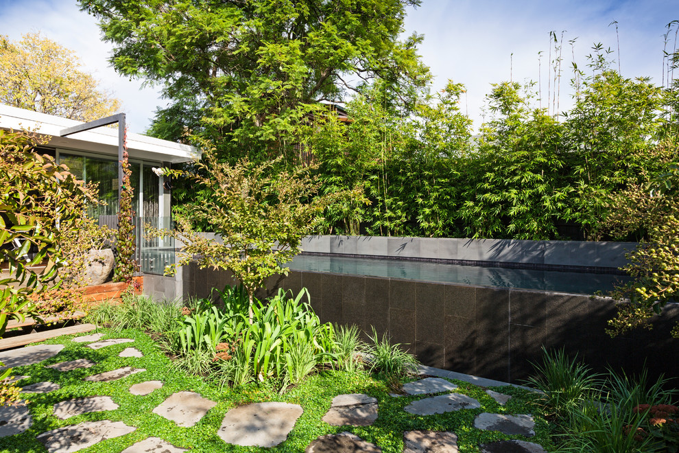 Imagen de piscina infinita asiática de tamaño medio rectangular en patio trasero con suelo de baldosas