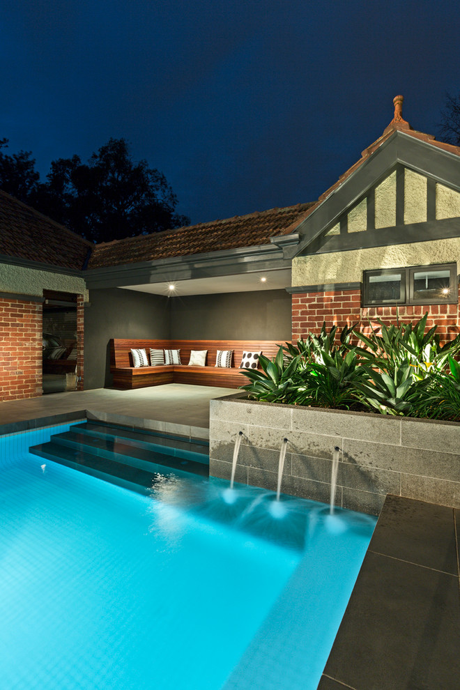 Modelo de piscina con fuente alargada tradicional de tamaño medio a medida en patio trasero con adoquines de piedra natural