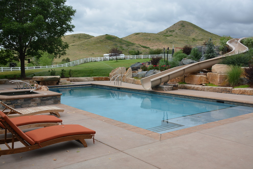 Modelo de piscina con tobogán alargada contemporánea grande rectangular en patio trasero con losas de hormigón