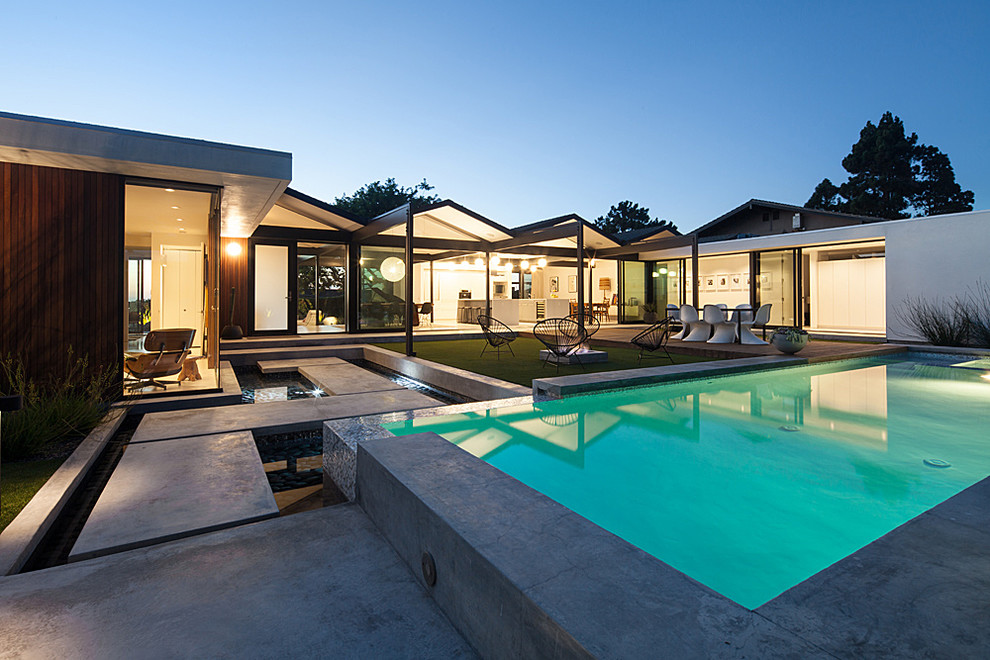 Esempio di una piscina monocorsia minimalista rettangolare di medie dimensioni e dietro casa con una vasca idromassaggio e lastre di cemento
