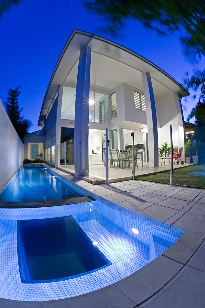 Imagen de piscina alargada actual en patio lateral con adoquines de piedra natural