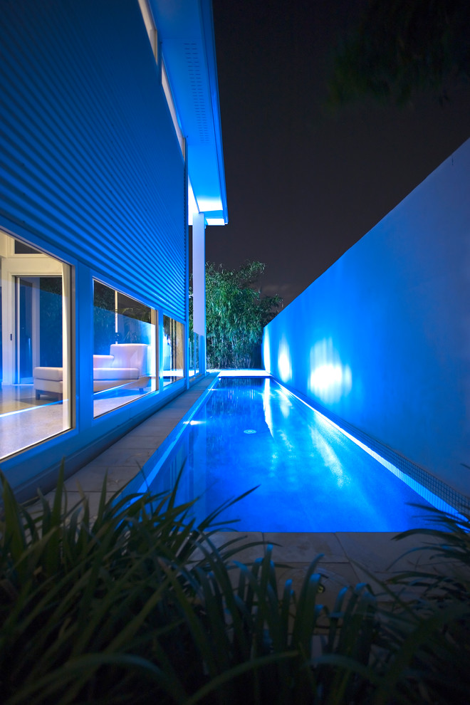 Diseño de piscina alargada actual en patio lateral con adoquines de piedra natural