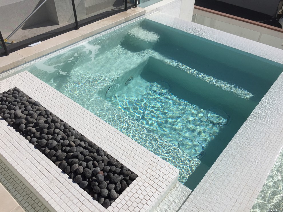 Cette photo montre une piscine à débordement et avant tendance de taille moyenne et rectangle avec un bain bouillonnant et une dalle de béton.
