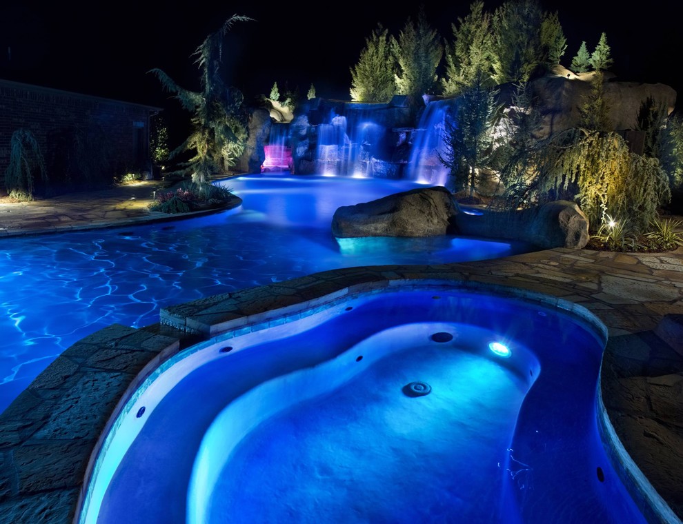 This is an example of an expansive rustic back custom shaped natural swimming pool in Oklahoma City with a water feature and natural stone paving.