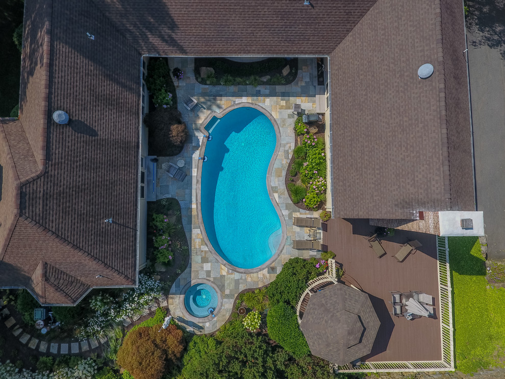 Ejemplo de piscinas y jacuzzis alargados tradicionales grandes tipo riñón en patio trasero con suelo de baldosas