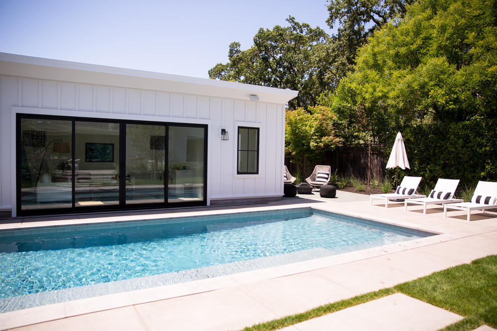 На фото: прямоугольный бассейн среднего размера на заднем дворе в стиле кантри с домиком у бассейна и мощением тротуарной плиткой