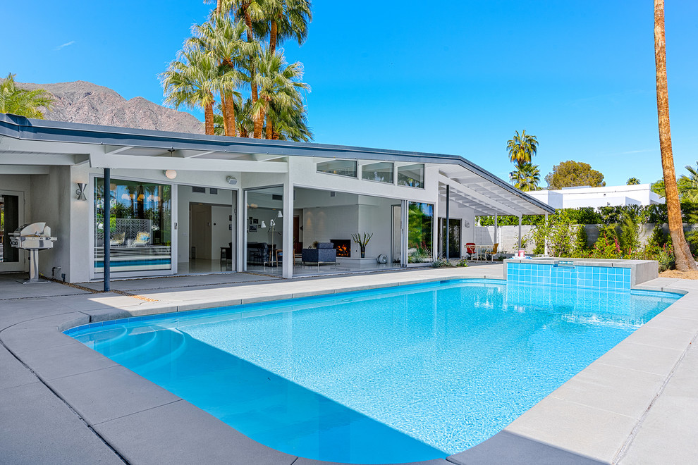 Foto de piscinas y jacuzzis alargados retro de tamaño medio rectangulares en patio trasero con losas de hormigón