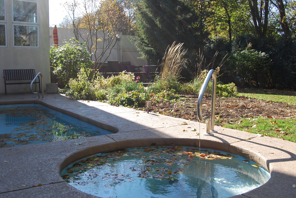 На фото: спортивный, угловой бассейн среднего размера на заднем дворе с джакузи и покрытием из каменной брусчатки