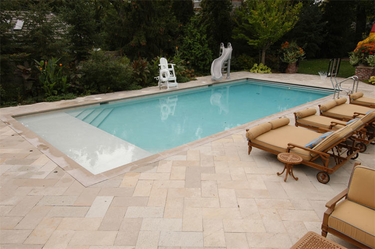 Modelo de piscina alargada clásica de tamaño medio rectangular en patio trasero con adoquines de piedra natural